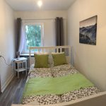 weißes Bett, 1,40m Breite, graue Bettwäsche, Zierkissen in grün und weiß, grüner Bettläufer, graue Gardinen, Laminatboden